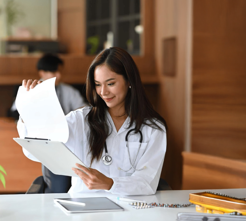 Partner with InvicieQ for proactive billing and revenue recovery Smiling female doctor reviewing patient billing documents in a clinic office setting